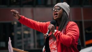 Chicago Teachers Union President Stacy Davis Gates in a red sweatshirt speaking into a microphone.